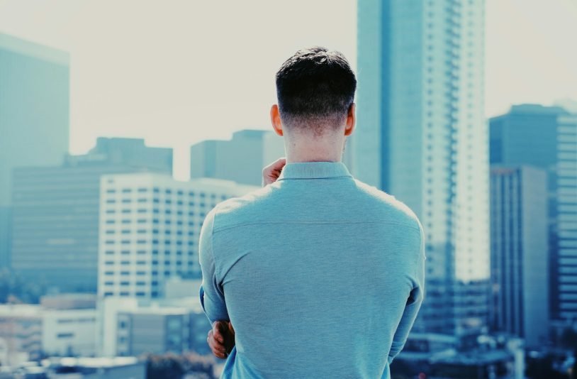 man in long sleeve shirt standing in front of city buildings